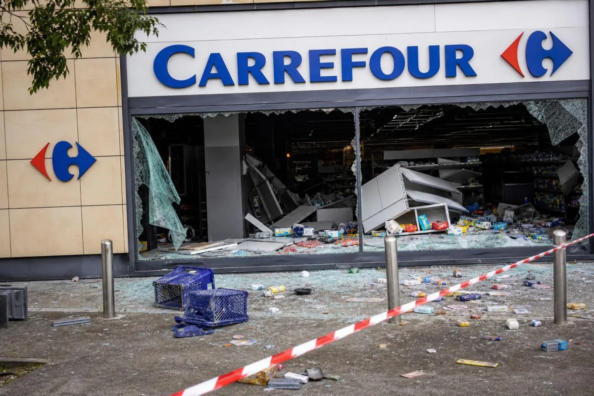Vetrina infranta del Carrefour con merce sparsa e nastro della polizia attorno all’area danneggiata